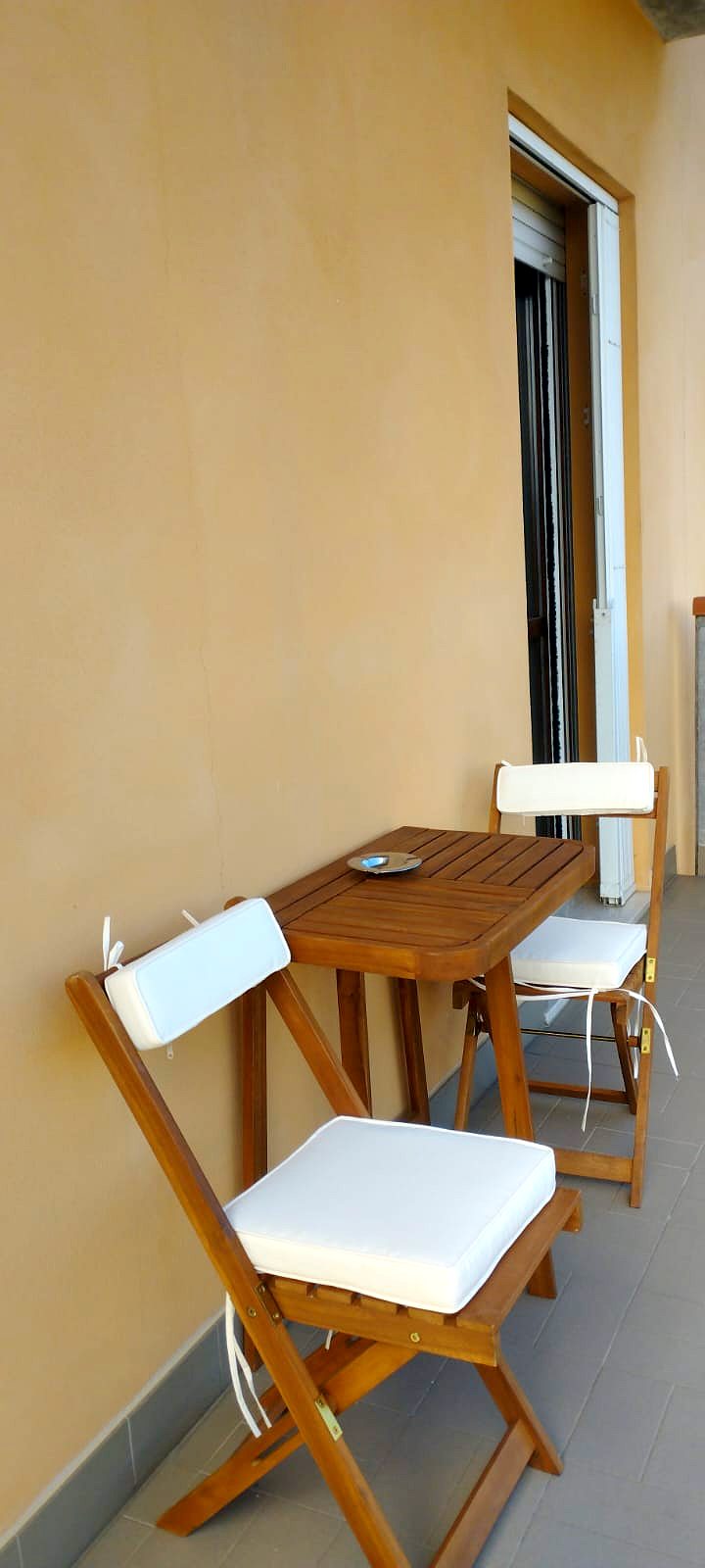 Il balcone di Casa Plac con tavolino e due sedie pieghevoli in legno con cuscini bianchi