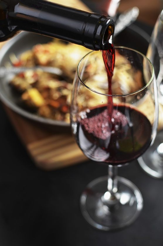 Vino rosso versato in un calice, con un piatto sullo sfondo