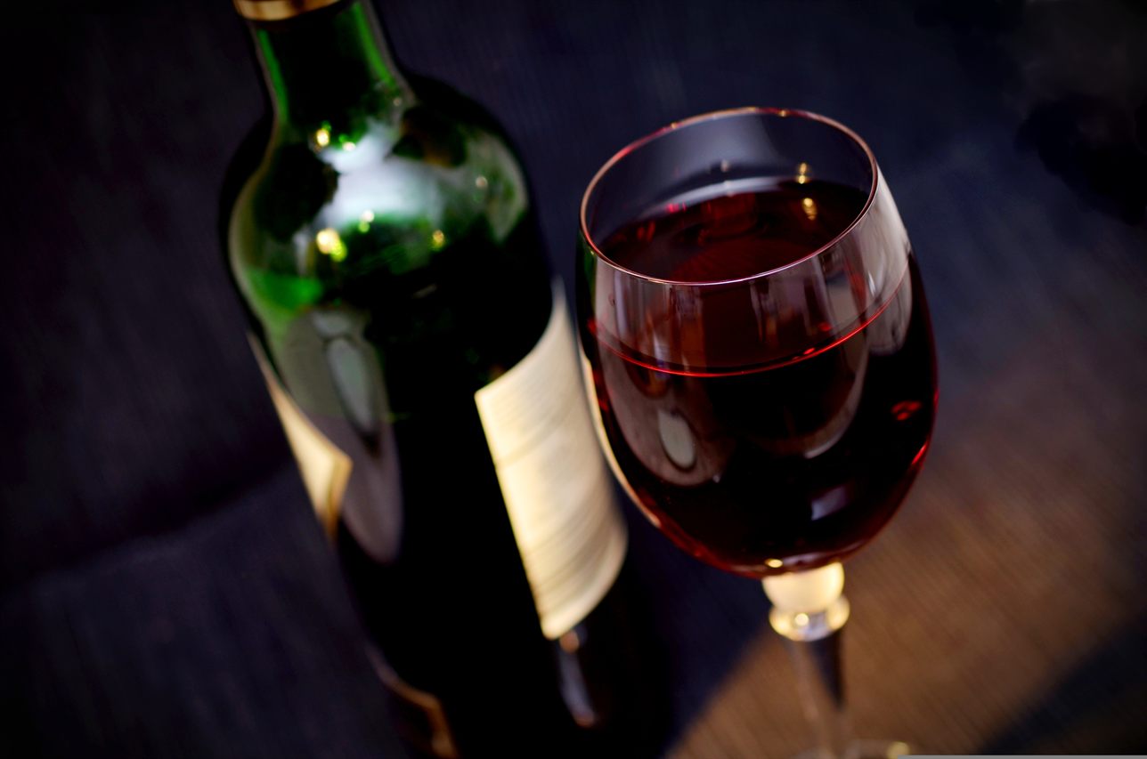 Un bicchiere di vino rosso, con la bottiglia sullo sfondo