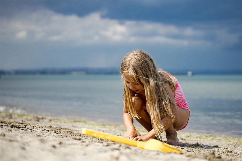 Una bambina gioca con la sabbia in riva al mare, con una paletta gialla