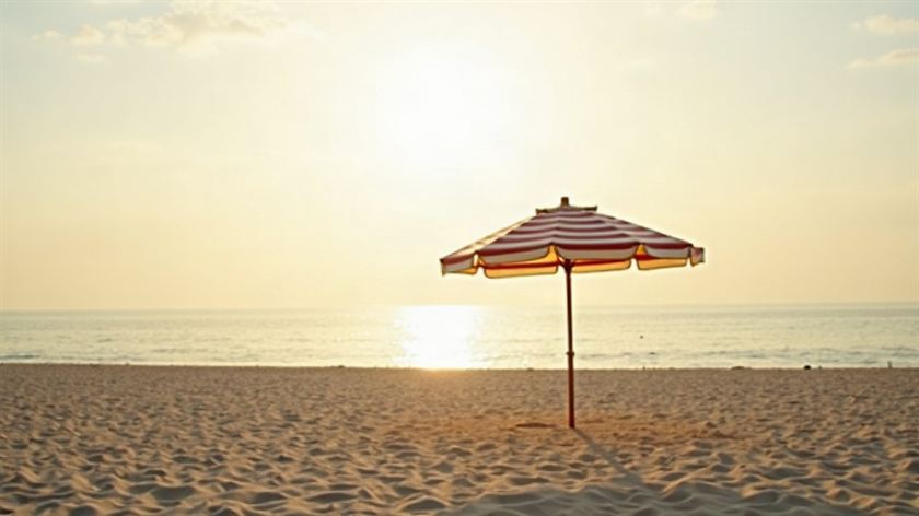 Un ombrellone a righe aperto su una spiaggia deserta, il mare calmo dietro nella luce bassa del pomeriggio